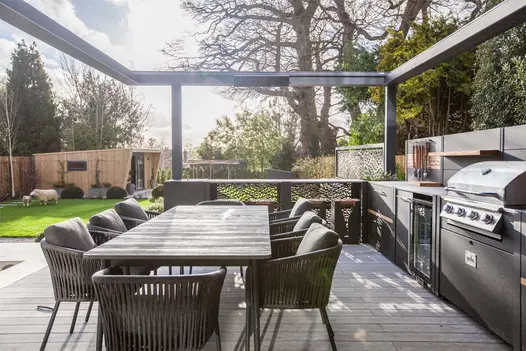Outdoor kitchen and dining area laid with Luna DesignBoard decking boards under open-roofed pergola. Built by Graduate Landscapes.