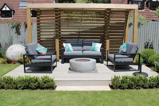 Lounge set with stone fire pit on Millboard Smoked Oak composite deck with pergola. Design by Outerspace Creative Landscaping.