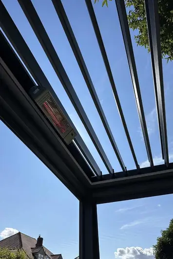 Close-up of the Deluxe Anthracite Grey metal Pergola's open louvres, framing a backdrop of trees and blue skies, available in 4x4.