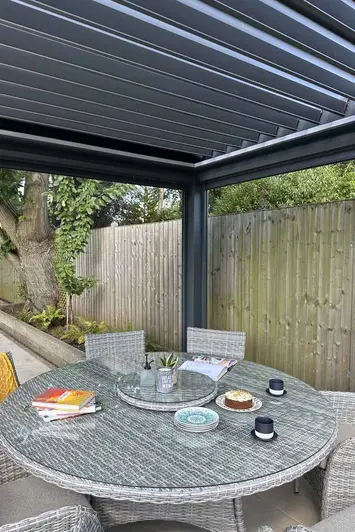 Close-up of the Anthracite Grey 3x3 Deluxe Pergola, showcasing the louvres open and light filtering through the slats onto a dining table.