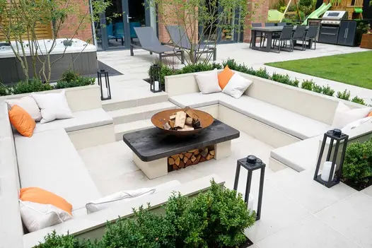 Porcelain Paving used around sunken seating area surrounded by planted copings clad in desert beige composite cladding, fire-pit in the middle.