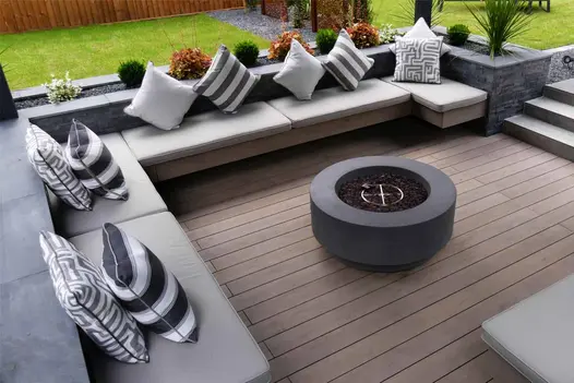 Corner shaped built in bench with planters surrounds fire pit sitting on traditional designboard composite decking.