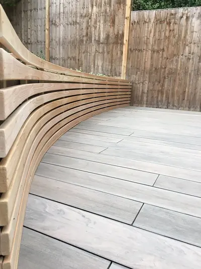 Curved wooden beams create a raised flowerbeds against rustic fencing, on Traditional Designboard Composite Decking.