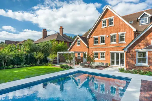Back garden of gabled house with patio in Dove Grey Smooth Sandstone paving and clay pavers, with pergola, lawn and swimming pool.