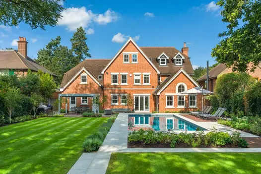 Dove Grey Sawn Sandstone paving surrounds blue-lined swimming pool, separating it from lawn, at back of large gabled house.