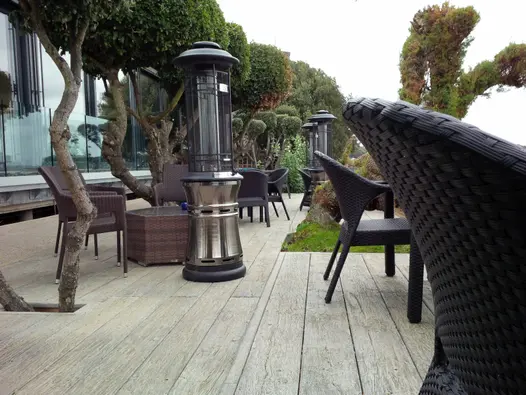 Long seating area with patio heaters, , with topiarised trees and rattan outdoor furniture sets on Driftwood Millboard decking. 