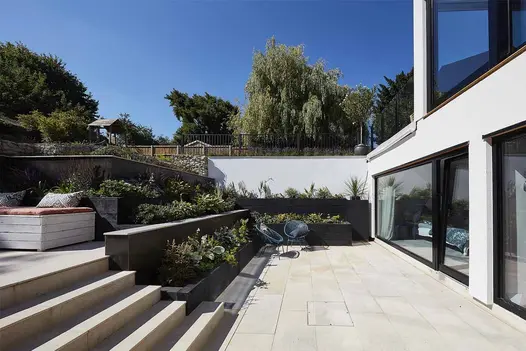 A sunken courtyard featuring three tiers of a modern garden, with bullnosed porcelain steps and retaining walls, complemented by planting behind.