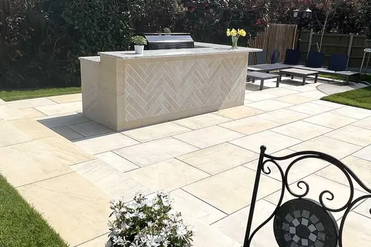 Outdoor kitchen counter with herringbone pattern front on patio of Harvest smooth sandstone paving, with seating area behind.