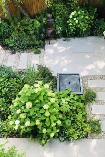 View from above sees Florence Grey Porcelain patio with staggered slabs between pebbles, green plants surrounds with square water feature in the middle.