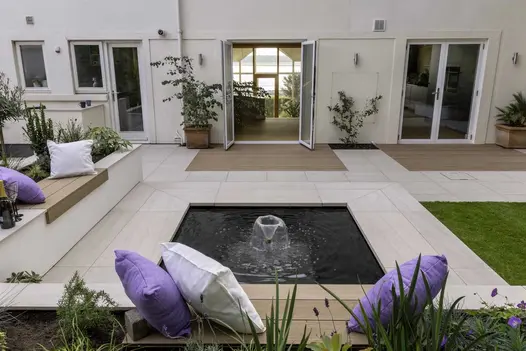 Fountain in midst of square pond with edges recessed beneath Faro porcelain coping with 40mm downstand, part of patio of house.