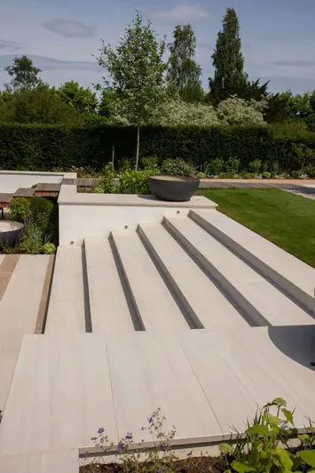 Faro porcelain wall coping stones top wall with steps leading up to a large lawn area, same material used for paving.