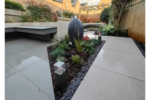 Cantilevered benches and sharp-angled beds in back garden fully paved in Polvere 800x800 and Trendy Black porcelain slabs.
