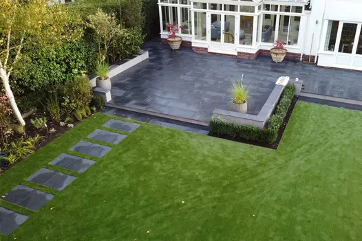 Patio in Florence Dark outdoor tiles, edged with low white wall, extends into lawn with paving slabs set as stepping stones.