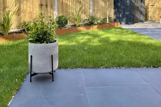 Circular garden planter on a Florence Dark Porcelain patio adjoining to a lawn in a small back garden.