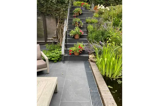 Small porcelain patio leading to a set of matching steps with extensive planning to the right hand side of the steps.