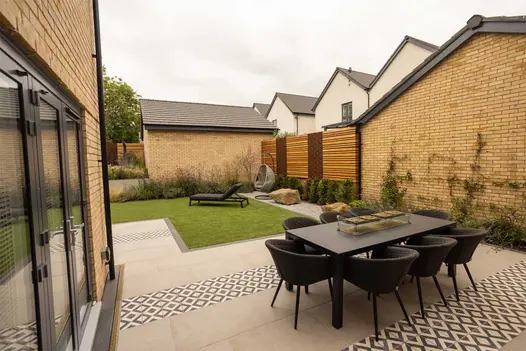 Outdoor dining set sits on patio of Florence Grey Porcelain paving with stripes of decorative tiles. Built by BRP Garden Services.