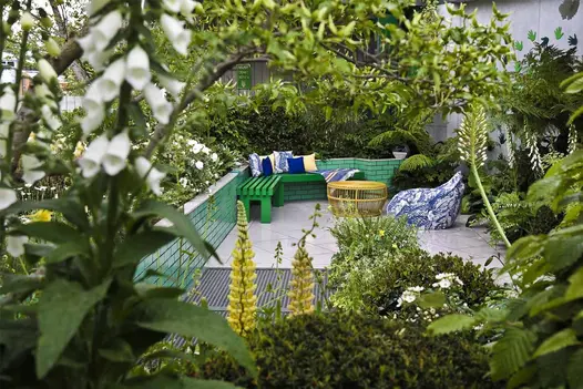 Ferns and white-flowered plants overhang Florence Grey porcelain paved seating area edged with green-tiled wall at RHS Chelsea.