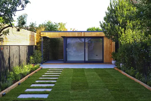 Spaced apart in lawn, Florence grey porcelain paving slabs lead to patio in front of garden office. Designed by Utopia Landscapes.