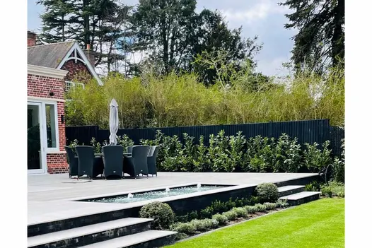 Large Florence grey porcelain patio with round dining set and parasol. Steps either side of rectangular pond descend to lawn.