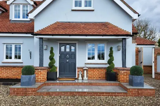 Wet Florence Storm Porcelain Paving, paired with 20mm bullnose steps, directs towards the front door, with topiary planting on both sides.