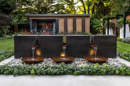 Low wall clad in Steel Dark DesignClad, perforated with 3 spouts dropping water into rusted bowls