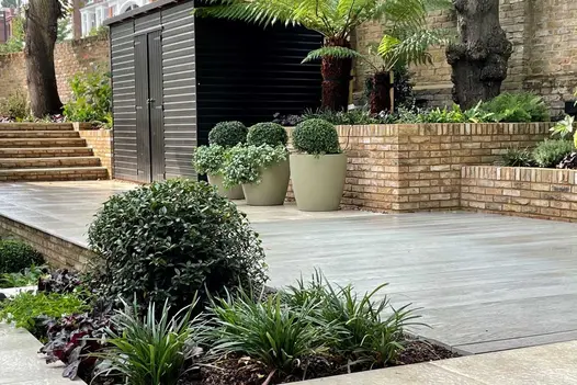 Walled garden with raised beds built of London Mixture facing bricks, next to 3 planters on raised area leading past shed to steps.