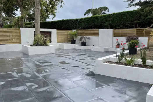 Wet Florence Dark Porcelain Paving paved around white rendered planting bays with clad fencing in the background.