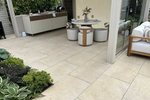 Jura Beige Porcelain 900x600 slabs laid under a metal pergola with outdoor kitchen bar and dining table and stools.