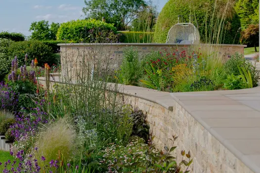 Terrace and wall edged with Buff Sawn Sandstone bullnose step treads, with colourful airy planting by Garden Solutions, Stroud.