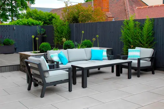Metal lounging set in a rear back garden paved with Polished Concrete porcelain in front of a raised composite decking area.