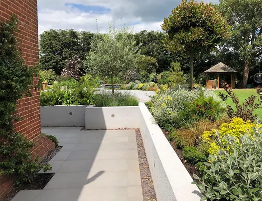 Path down the side of house paved in Steel Grey porcelain with retaining walls leading to an upper terrace of lawn and planting.