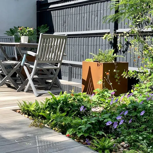 Steel corten planter sits on wet luna designboard composite decking with wooden table and chairs in the background.