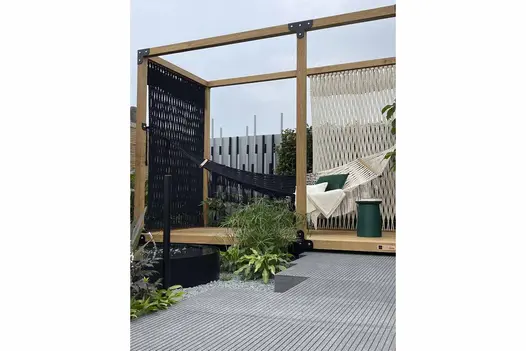 Black and white hammock hangs in wooden frame partially sitting on Black granite paving with narrow grooves cut into surface.