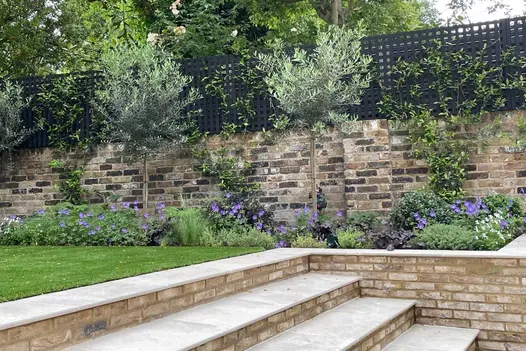 4 Gea porcelain 20mm bullnose steps with risers and flanking walls in London brick rise to walled lawn area with planted border.