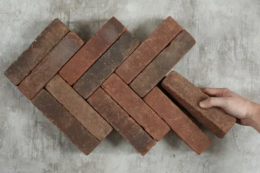 Hand places single Antique Red clay paver against 11 laid herringbone on light background. Free UK delivery available.