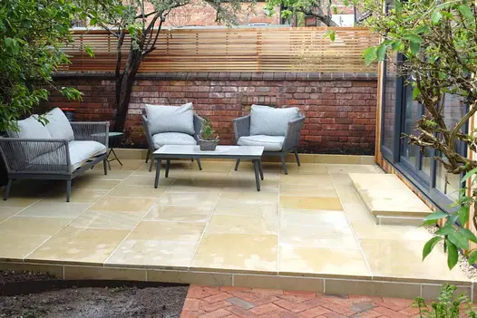 A back garden with Harvest Edging Stones, matching paving, and bullnose steps in warm pastel colours, leading to an outhouse.
