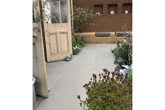 Adobe-style brick wall edges patio of Heath Sawn sandstone slabs. Lush planting and open french doors. Design by Jessica Makins.