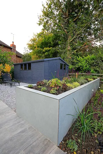 Large grey garden shed in gravel area of garden with long raised bed faced with Hydra Plomo luxury porcelain cladding.