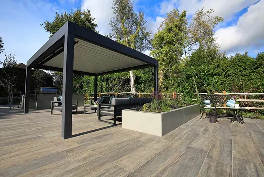 Large rectangular raised bed faced with Hydra Plomo external porcelain cladding next to metal pergola and outdoor furniture.