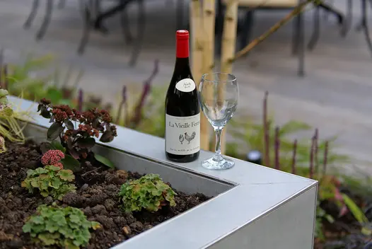 Wine glass and bottle stand on edge of planted raised bed completely faced with Hydra Plomo Designclad. Furniture in background.