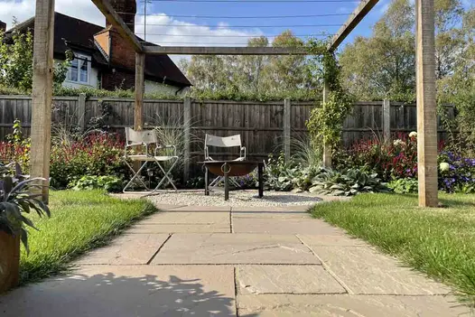 Beneath wooden pergola wide path of Raj Green sandstone slabs leads to gravel circle with seating. Built by JG Landscaping.