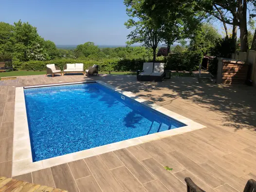 Swimming pool on a hot summers day with Rovere wood effect porcelain paving laid around looking out across beautiful countryside.