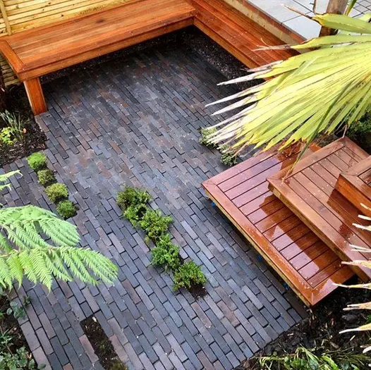 View down to 3 intersecting square wooden steps descending to small area  paved with Ancona Dutch clay pavers, with inbuilt bench.