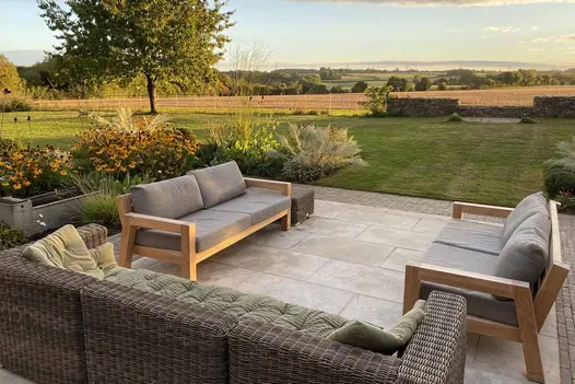 3 outdoor sofas on Jura Beige limestone slabs edged with clay pavers in large lawned garden with uninterrupted view of fields.