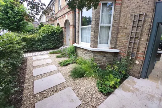 Front garden of period terrace house, with shrub border and gravel set with widely separated Jura Beige sawn limestone slabs.