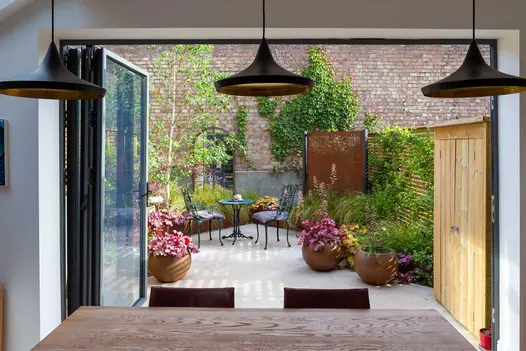 Bifold doors open onto Jura Beige Sawn limestone paved garden with pots of heucheras. Design by Sarah Kay. Built by Acacia Gardens.