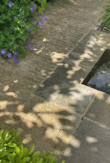Shadows cast over westminster clay paver bricks and raj green sandstone with foliage surrounding a water feature.