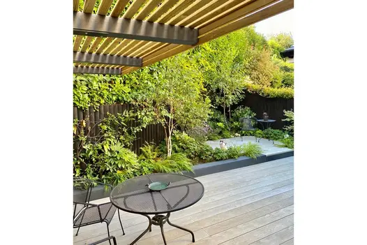 Aluminium table and chair on Smoked Oak Millboard decking next to mixed border and step up to small patio with seated cat.