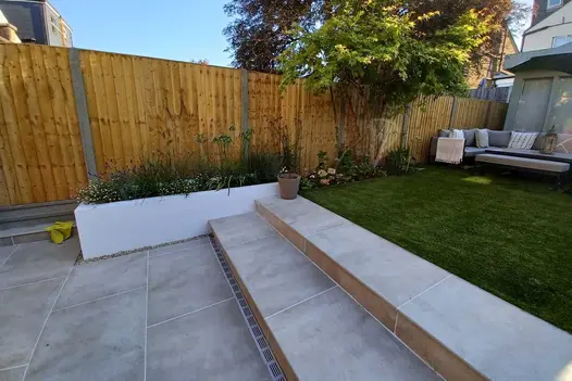 2 Cream porcelain outdoor steps rise from patio to lawn between white rendered raised beds. Design by Kingston Landscape Group.