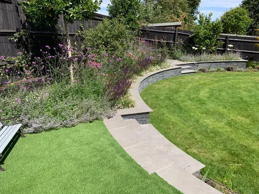 Large circular lawn bordered by curved retaining wall and steps. Steps and wall copings made from Steel Grey porcelain.